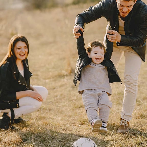 Mum and dad playing football with little boy outside