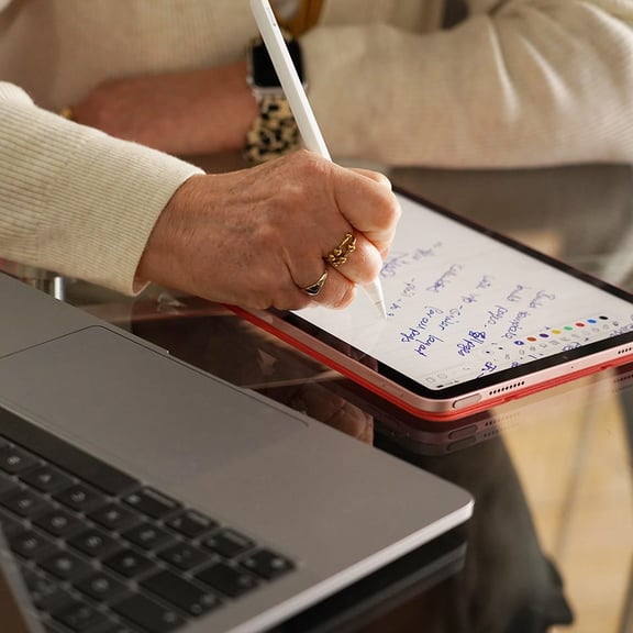 person writing on notebook next to laptop