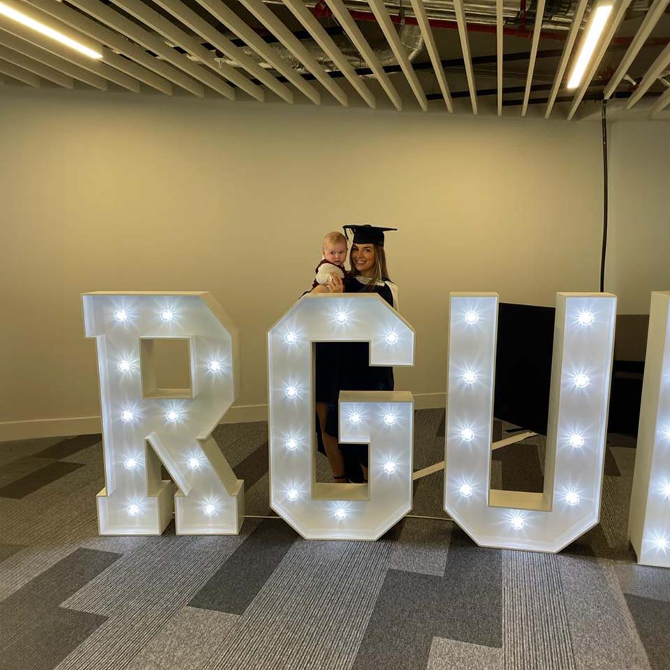 Amy at graduation in front of RGU sign