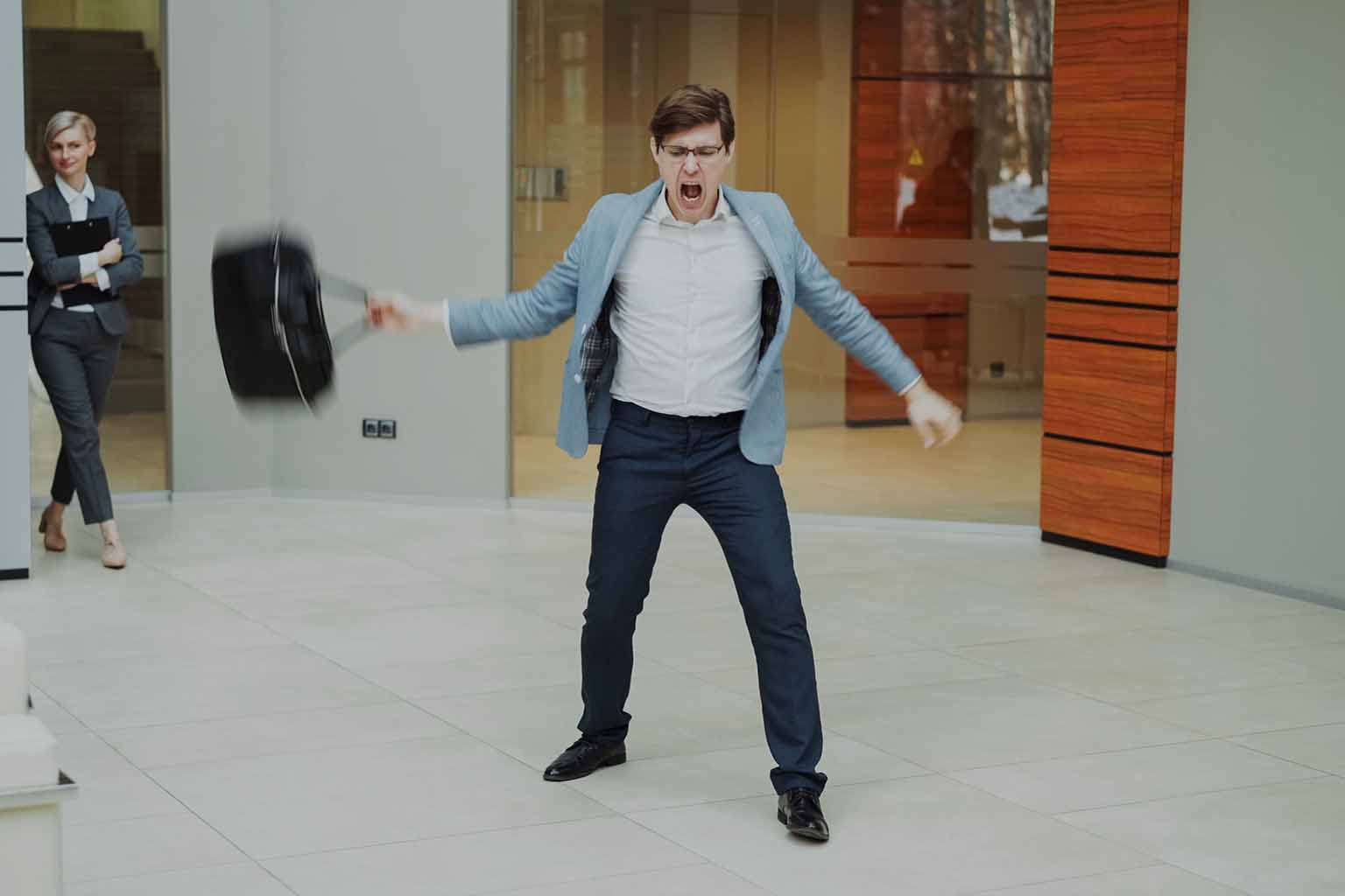 A man expressing frustration in a quiet hall, shouting and swinging his briefcase with his right hand