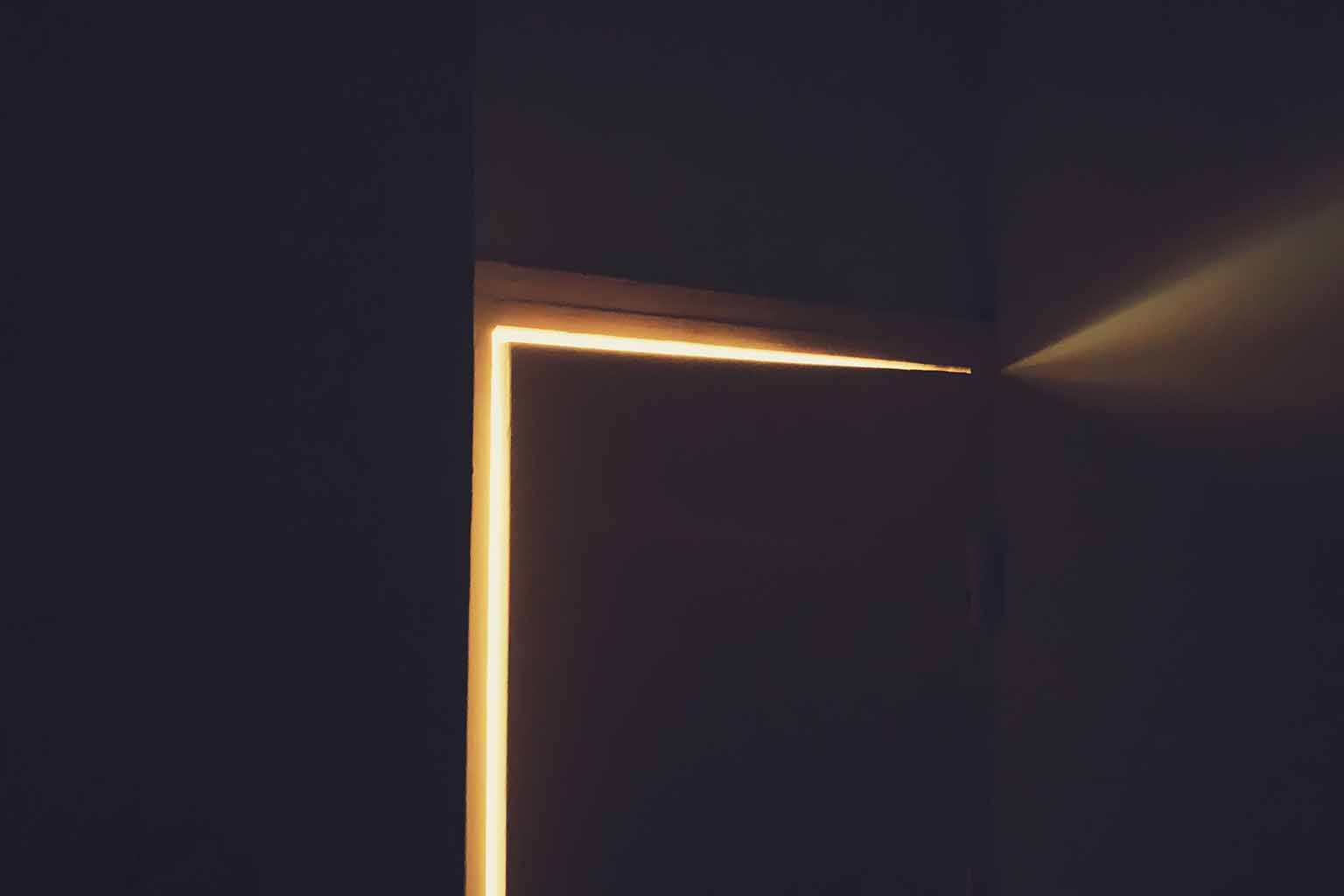 An ajar door letting a gold light into a barely lit room