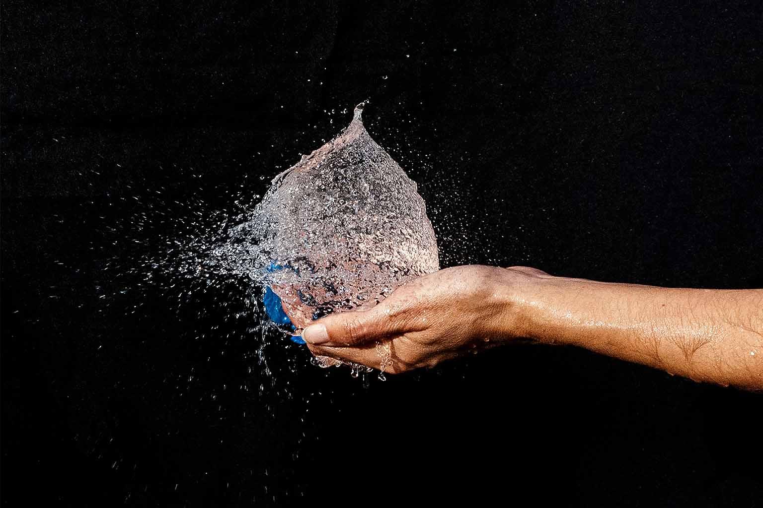 A balloon filled with water bursts in the palm of a hand