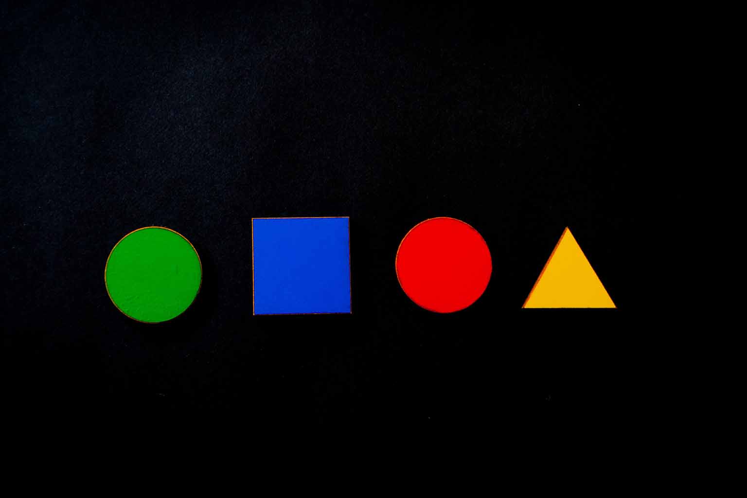 A green circle, blue square, red cicle and yellow triangle ordered in a line over a black background