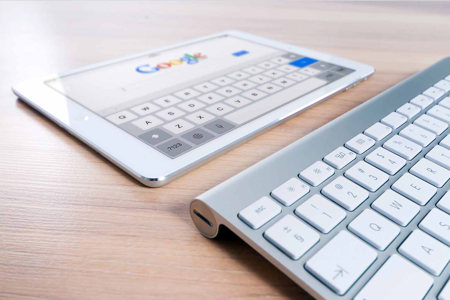 Close-up image of an Apple keyboard paired with a tablet displaying a Google web interface
