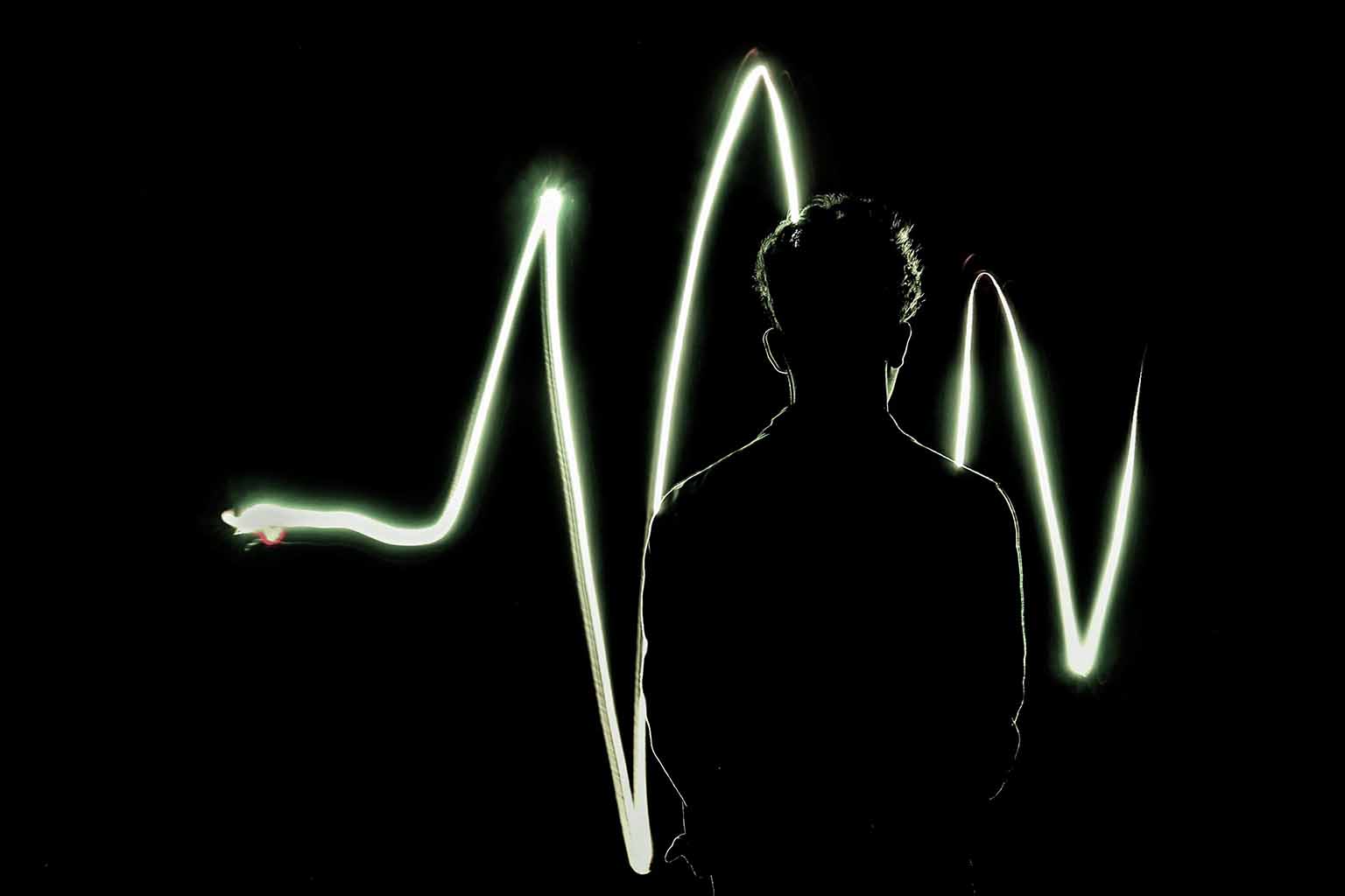 The silhouette of a man stands back to the camera with a light drawn audiowave in the background