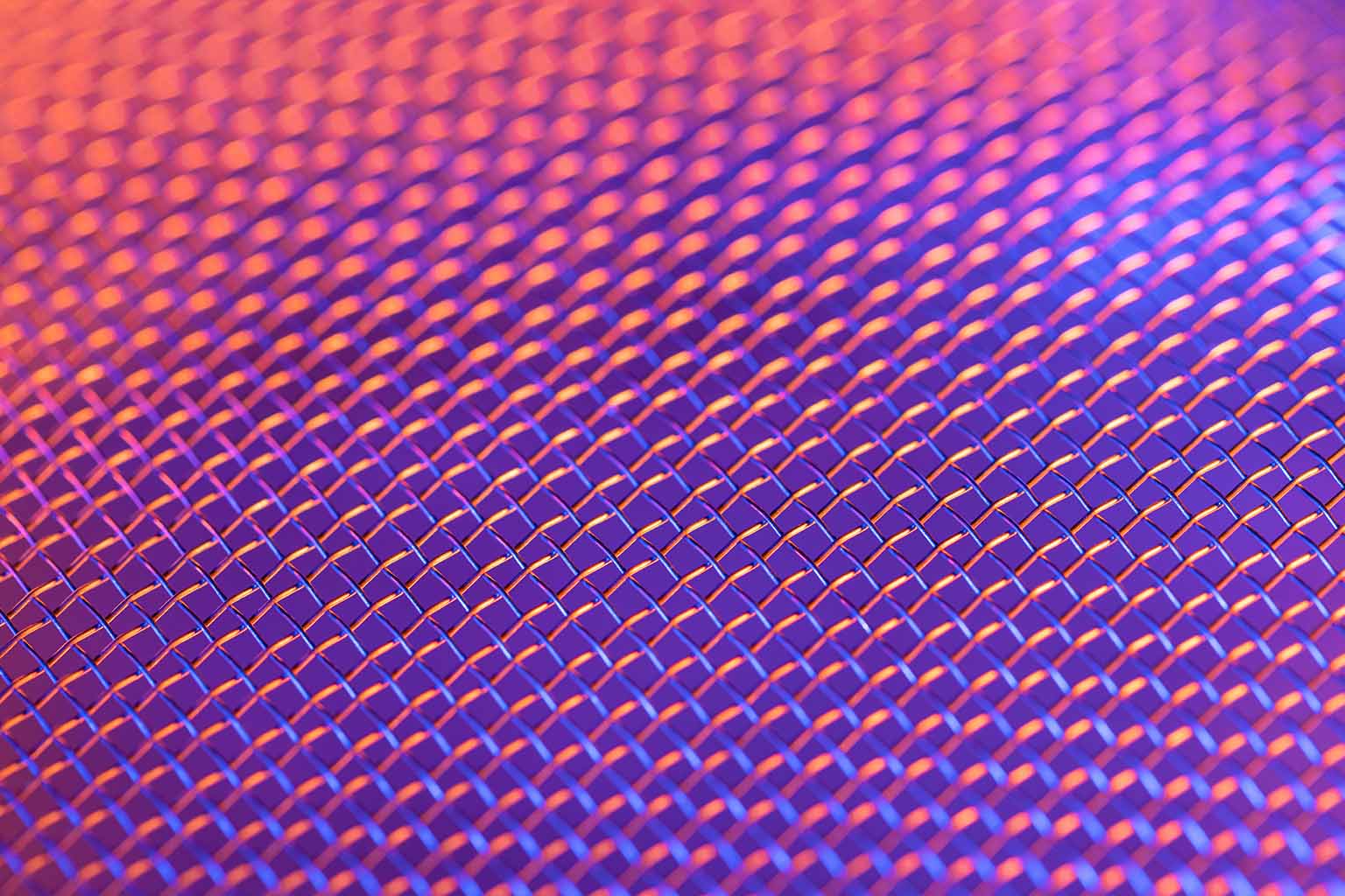 Close-up image of a microphone grille lluminated by pink and purple lighting tones