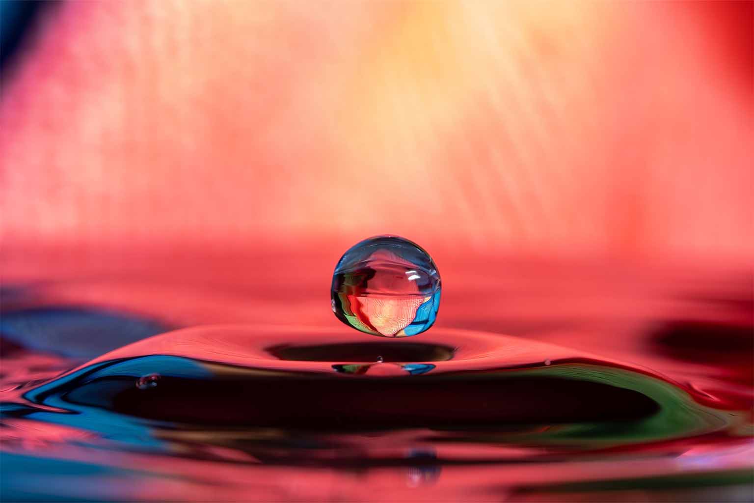 A levitating droplet lit up by red light with blue and green accents
