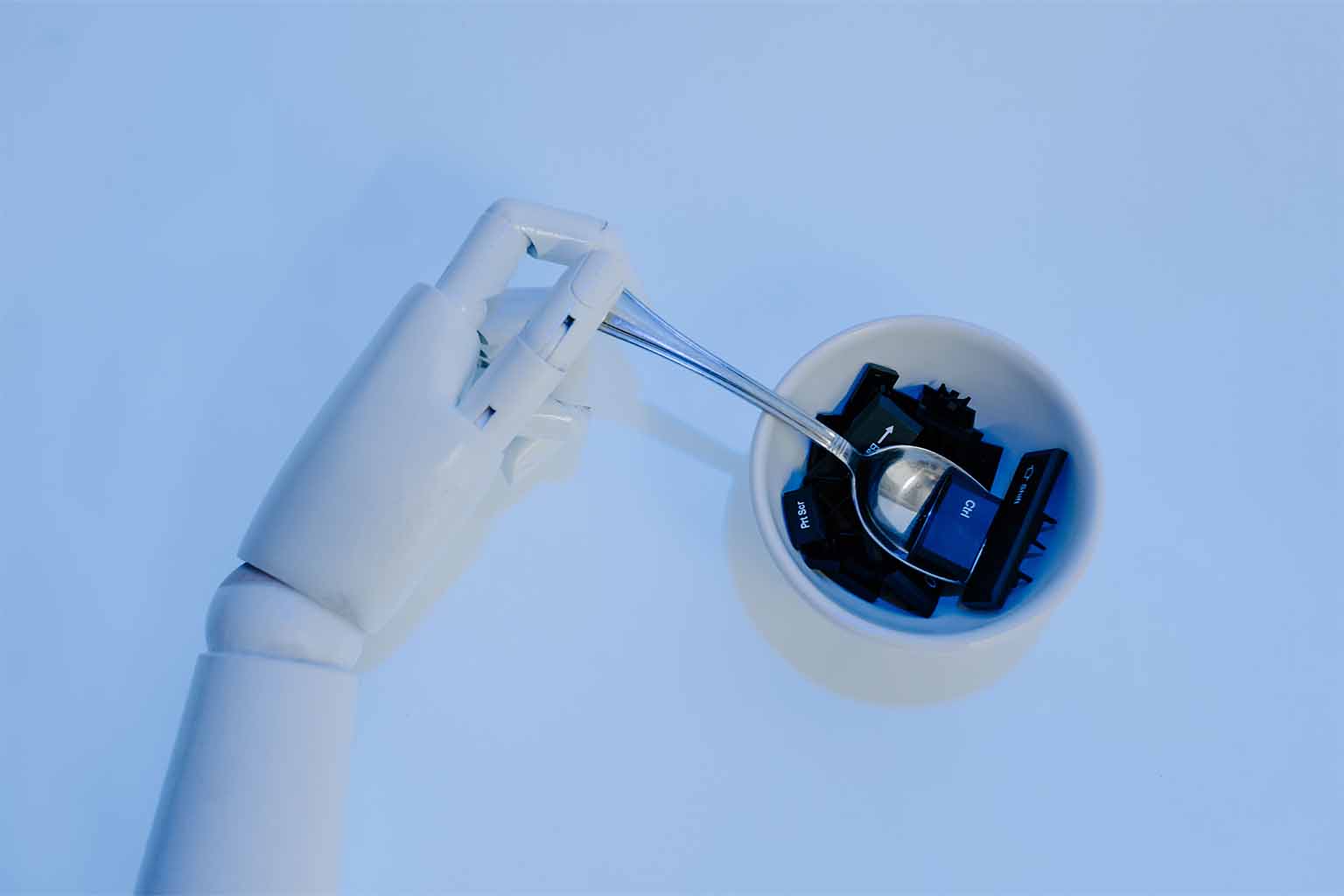 A robotic hand holding a spoon over a bowl filled with keyboard keys
