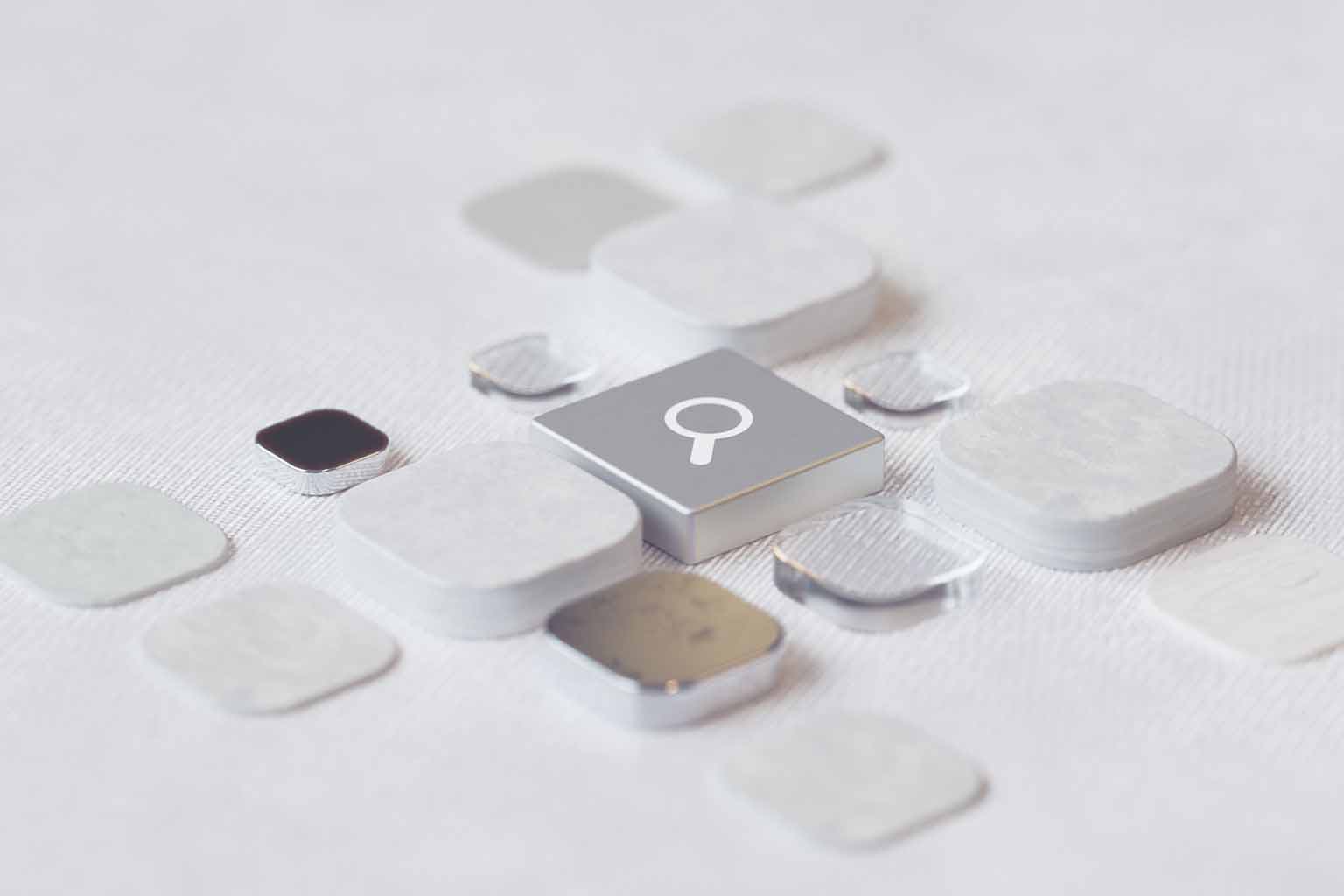 A silver tile featuring a white magnifying glass icon is surrounded by generic tiles of different shapes and colours against a white background