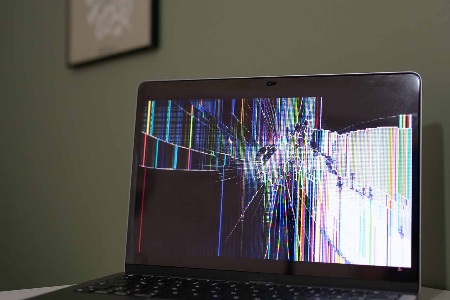 A laptop with a smashed screen sitting on a desktop