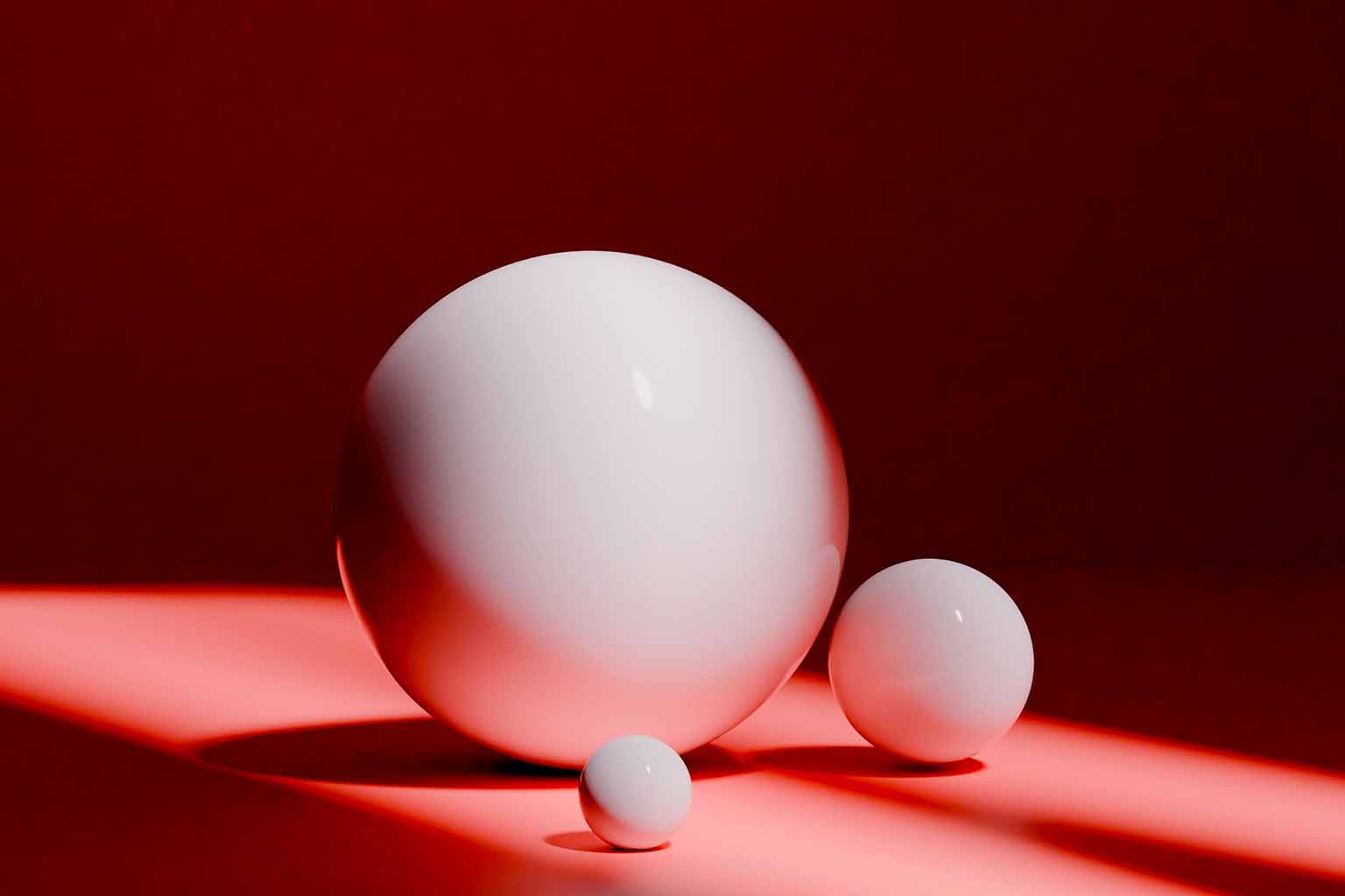 Three white glass marbles of different size positioned next to one another over a red background