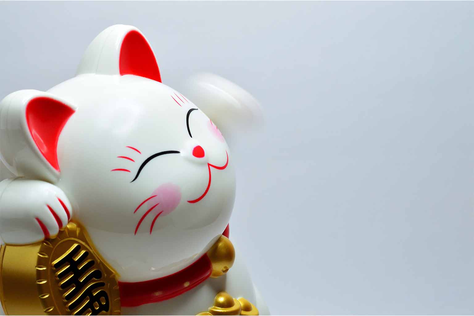 A white maneki-neko with a blurry, fast moving paw against a light grey background