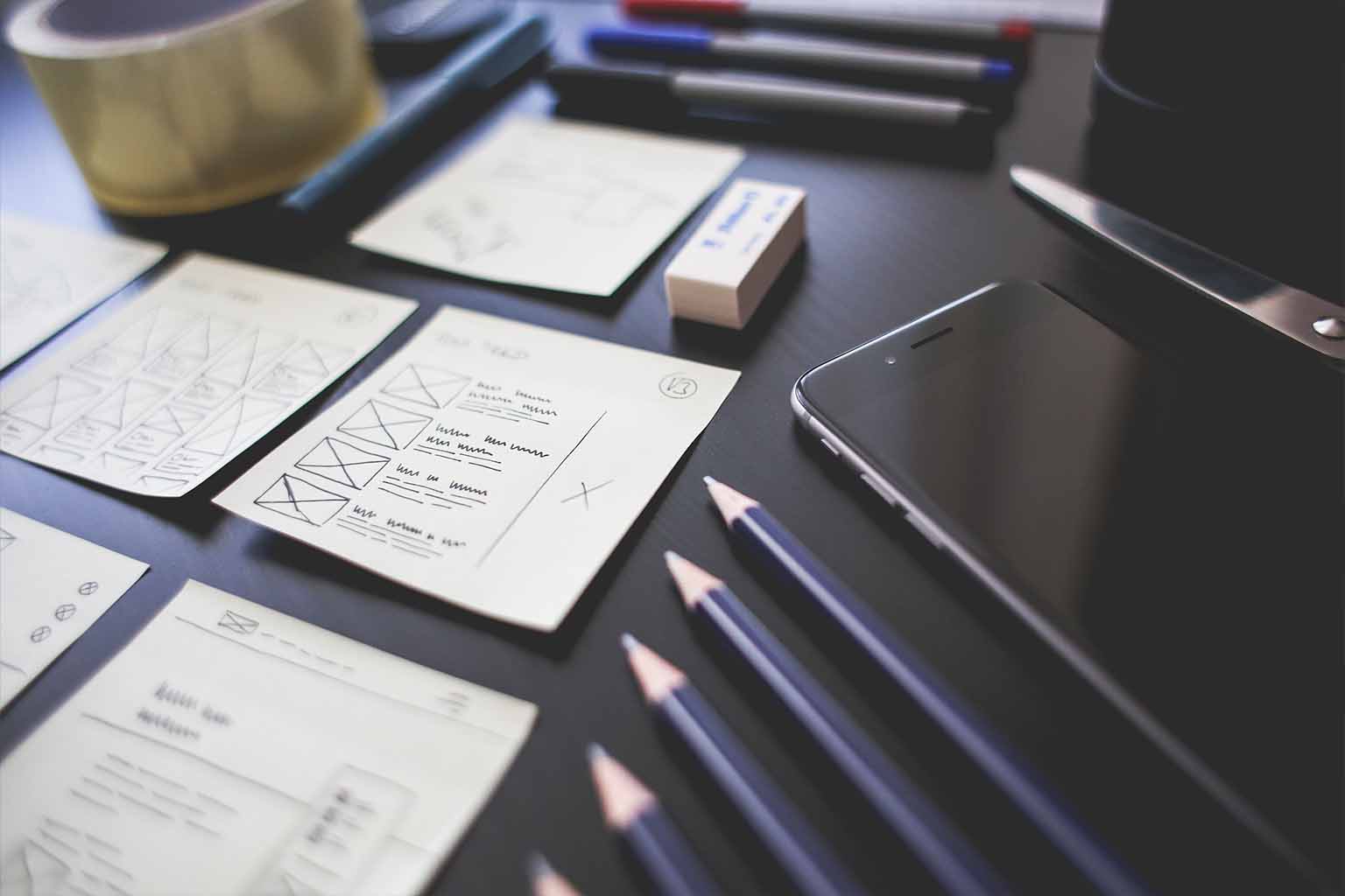 A tidy desktop where pencils, smartphones and paper drawn wireframes are neatly ordered