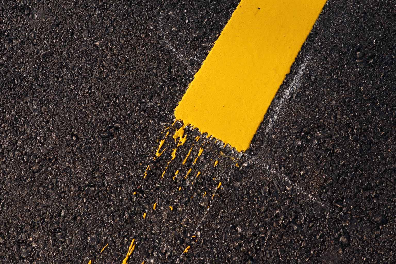 A yellow thermoplastic road marking against a dark road surface