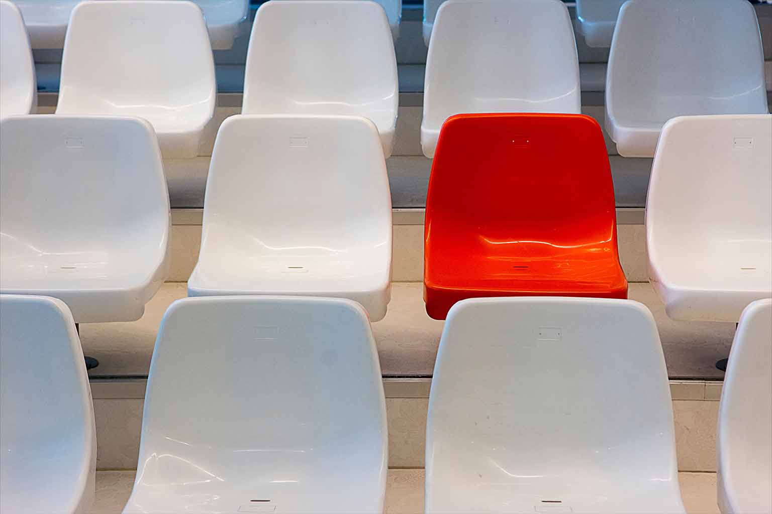 Three rows of white seats with a single contrasting red seat located at the centre of the middle row